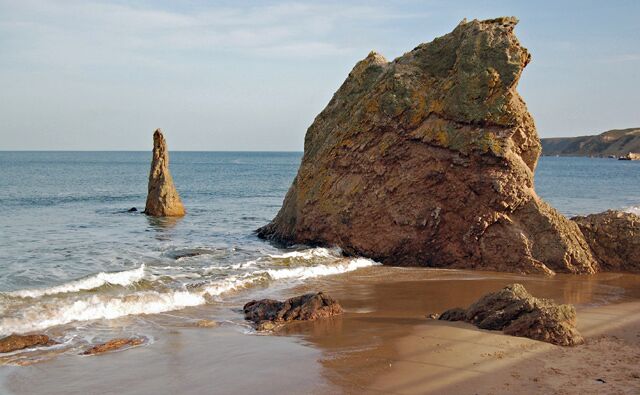 A rocky coastline with large boulders and a conical rock formation in the water.