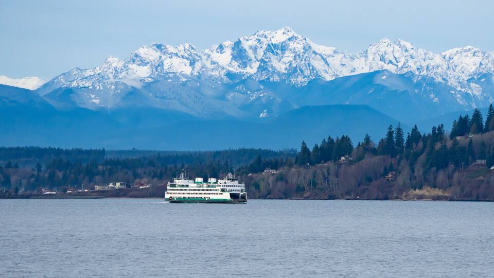 A ferry on a calm lake with snow-capped mountains in the background.