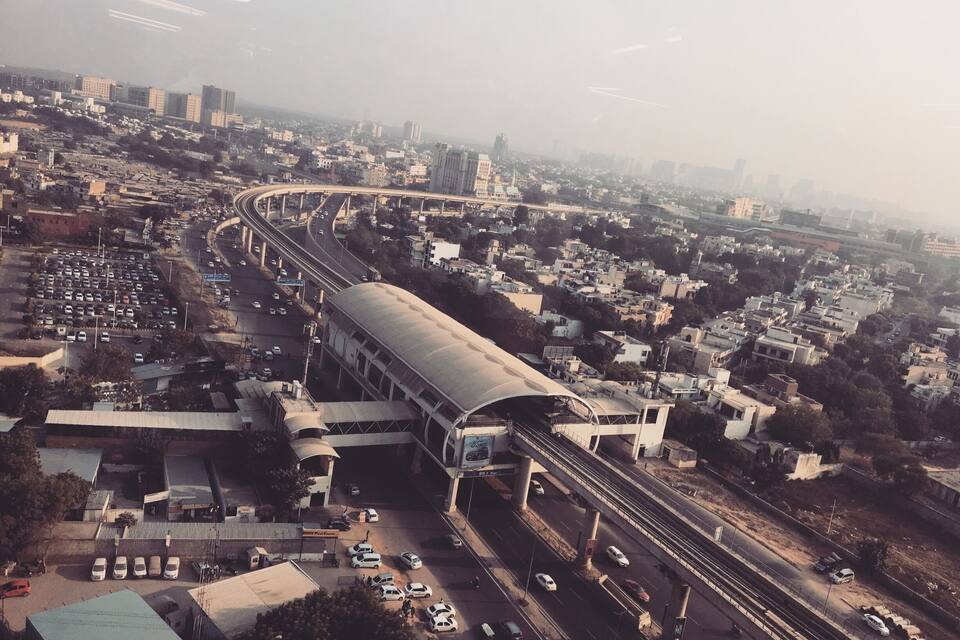 An aerial view of a city with a prominent curved bridge, a large parking lot, and dense urban buildings.