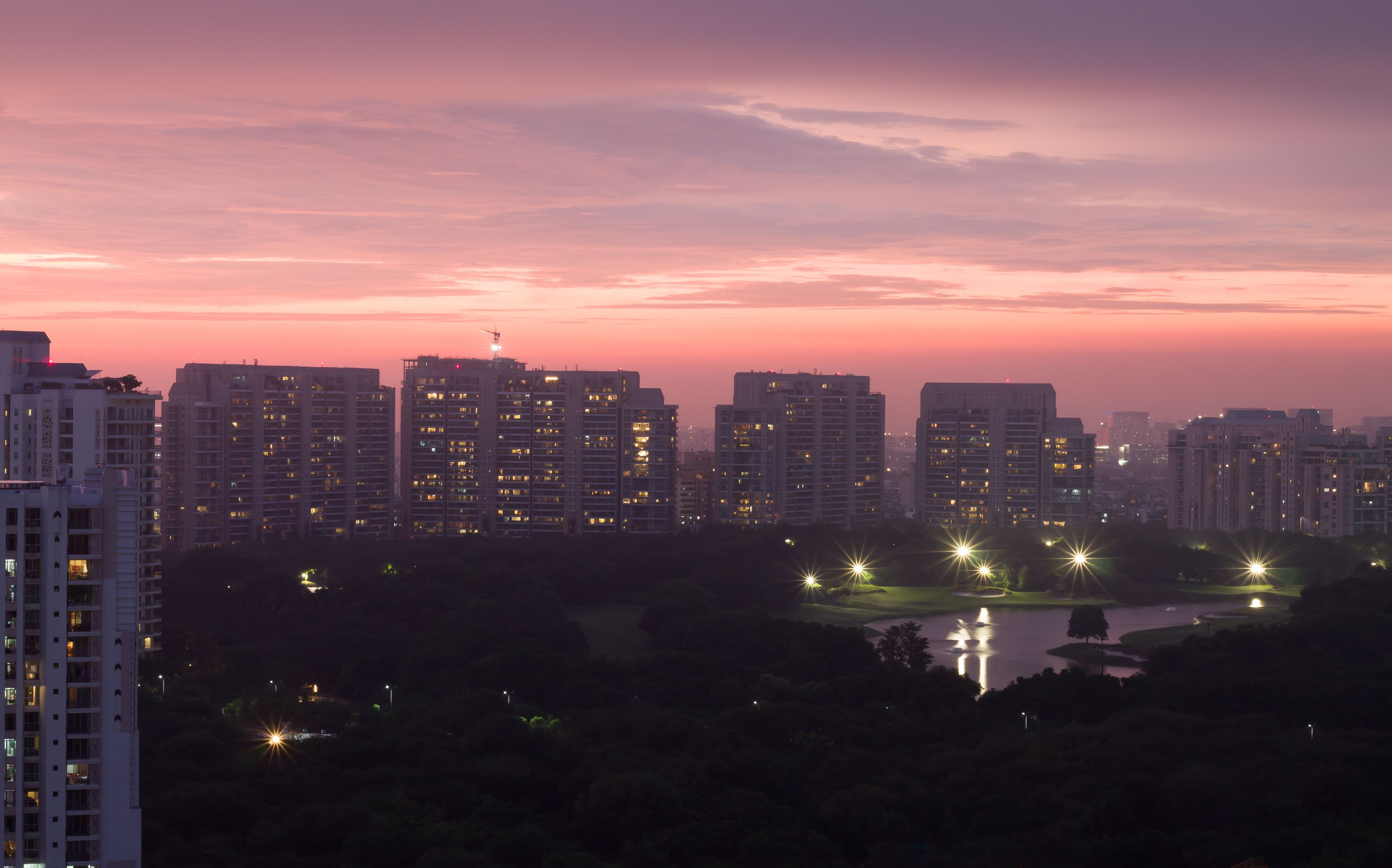 A city skyline at dusk with illuminated buildings and a calm lake reflecting the lights.