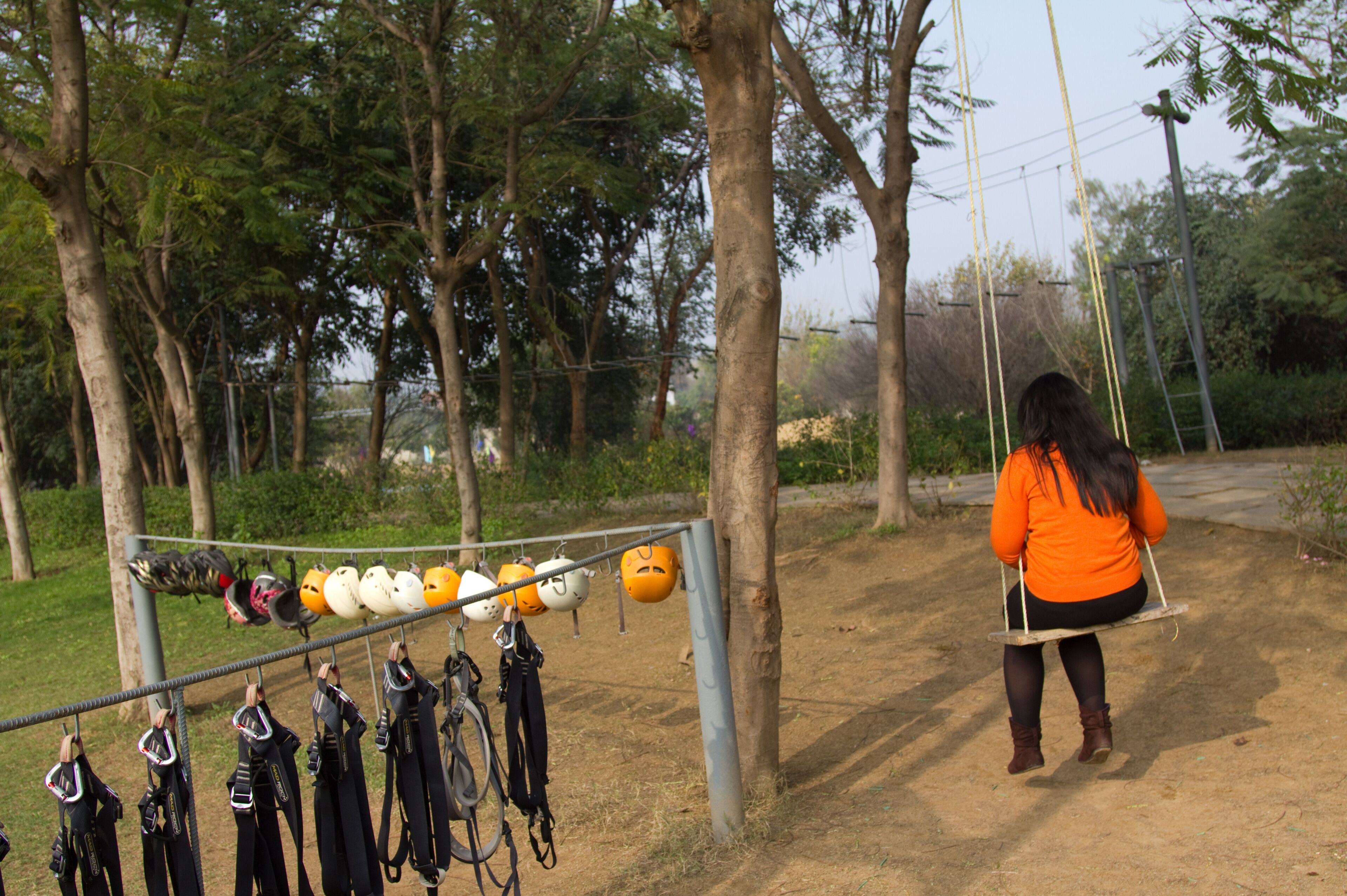 Indian woman with long hair wearing an orange top and black skirt sitting on a swing at a resort on the outskirts of Gurgaon, Haryana (India)