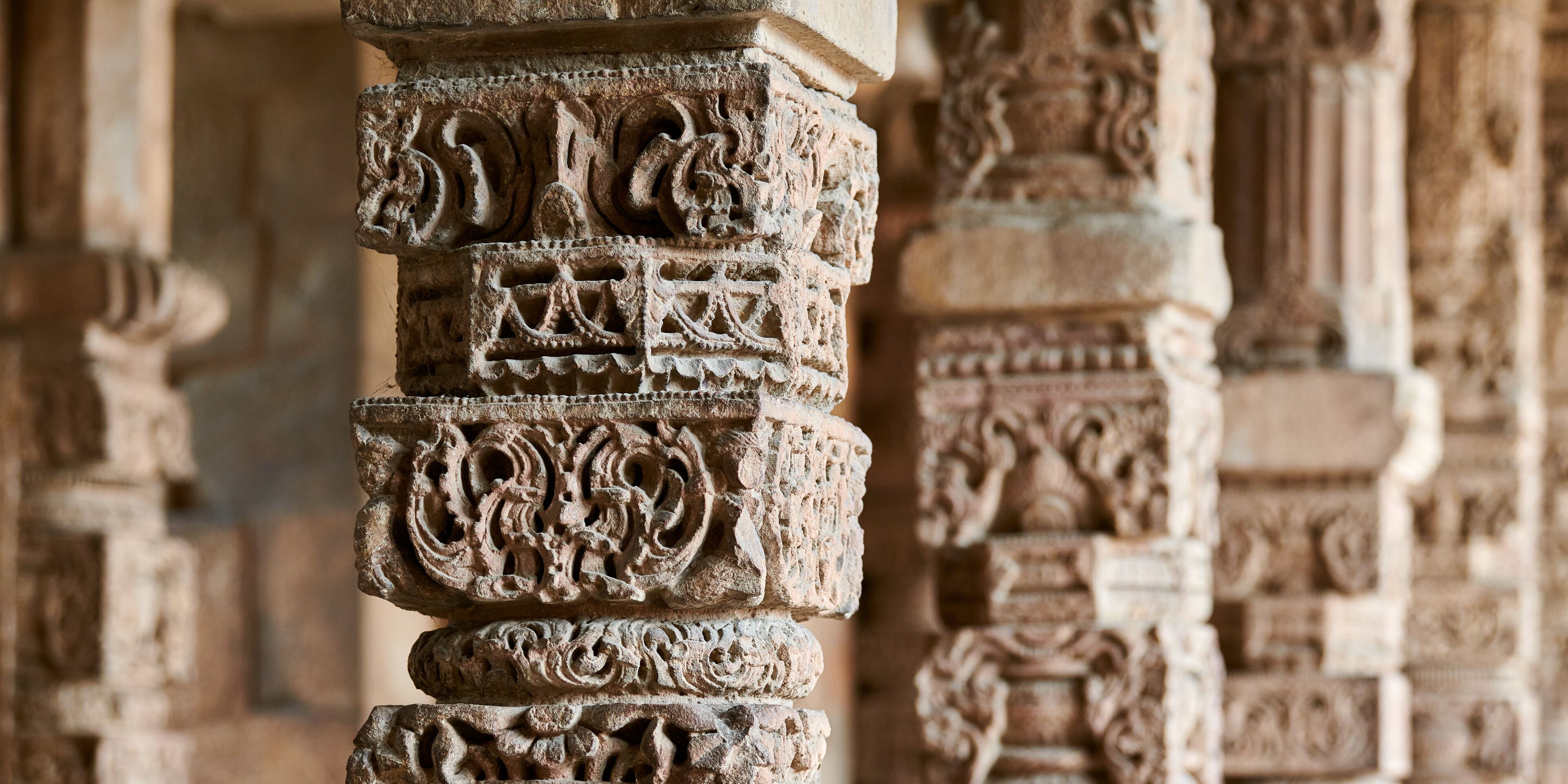 Stone columns with decorative bas relief of Qutb complex in South Delhi, India, close up pillars in ancient ruins of mosque landmark, popular touristic spot in New Delhi, ancient indian architecture