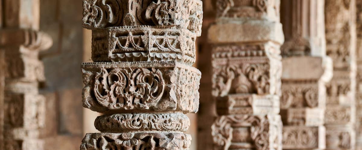 Stone columns with decorative bas relief of Qutb complex in South Delhi, India, close up pillars in ancient ruins of mosque landmark, popular touristic spot in New Delhi, ancient indian architecture