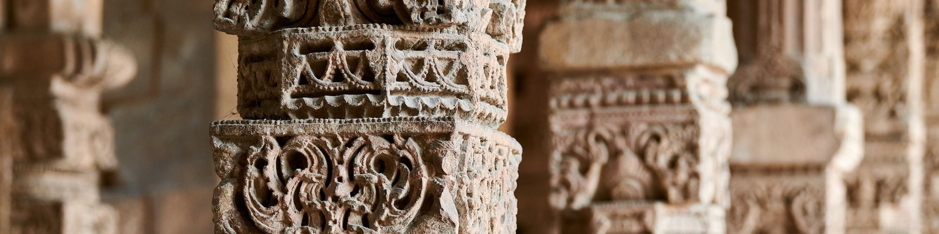 Stone columns with decorative bas relief of Qutb complex in South Delhi, India, close up pillars in ancient ruins of mosque landmark, popular touristic spot in New Delhi, ancient indian architecture