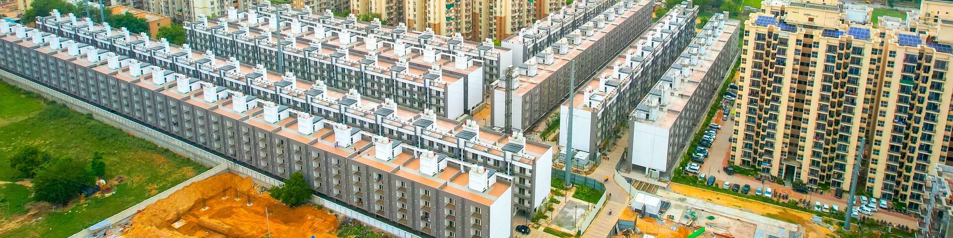 aerial drone shot symmetrically placed flats, houses, with skyscrapers at the back showing mass produced modular homes growing the real estate segment