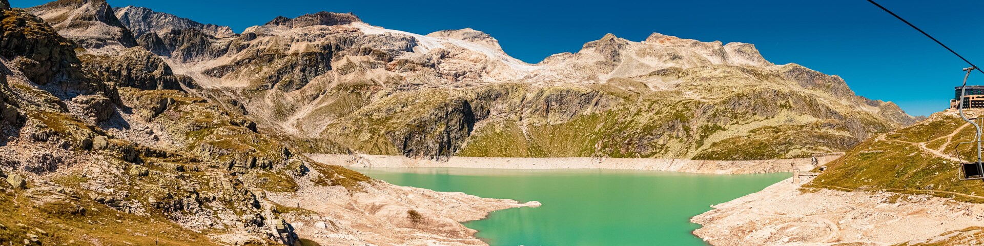 A mountain landscape with a turquoise lake, rocky terrain, and a cable car system.