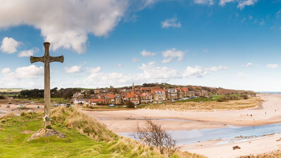 A coastal town with a prominent wooden cross, sandy beaches, and a river.