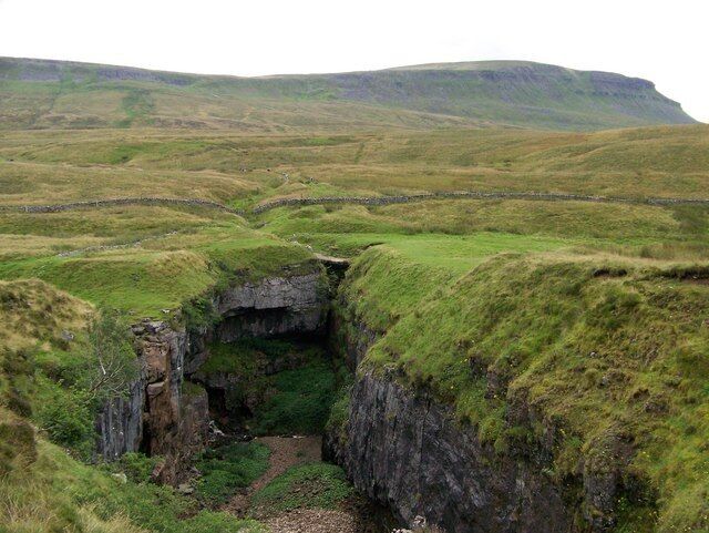 A grassy landscape with a rocky cave entrance.