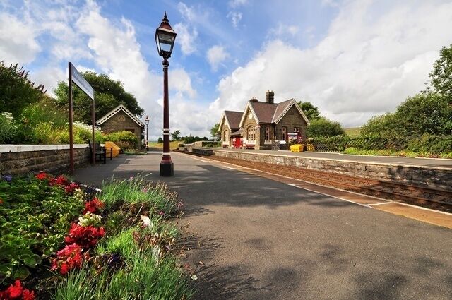 A railway station platform with a lamppost, flower beds, and traditional buildings.