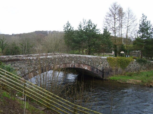 A stone bridge over a river with trees and hills in the background.