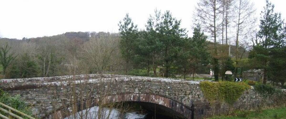 A stone bridge over a river with trees and hills in the background.