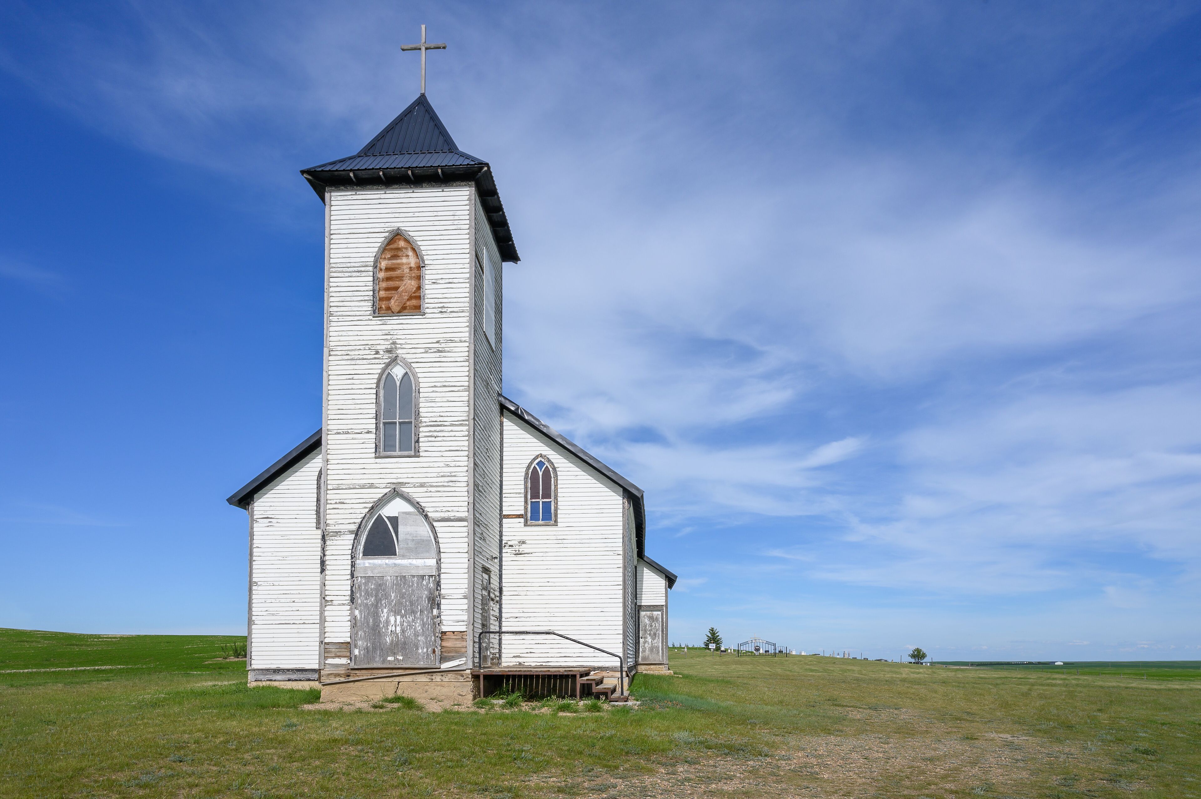 A white church with a cross on top, set in a grassy field under a clear sky.