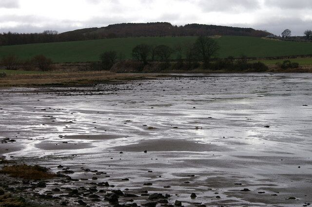 A river with rocks and a green hill in the background.