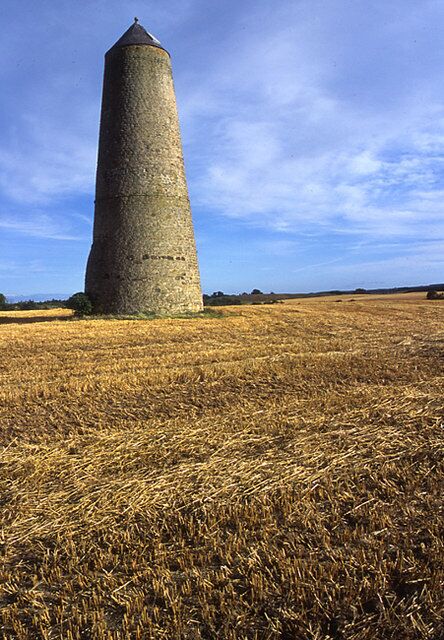 A tall stone tower in a field of golden wheat under a clear sky.