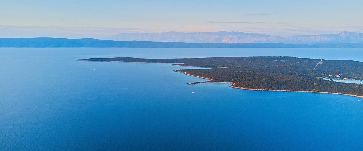 A coastal landscape with a large body of water, a small island with dense vegetation, and distant mountains.