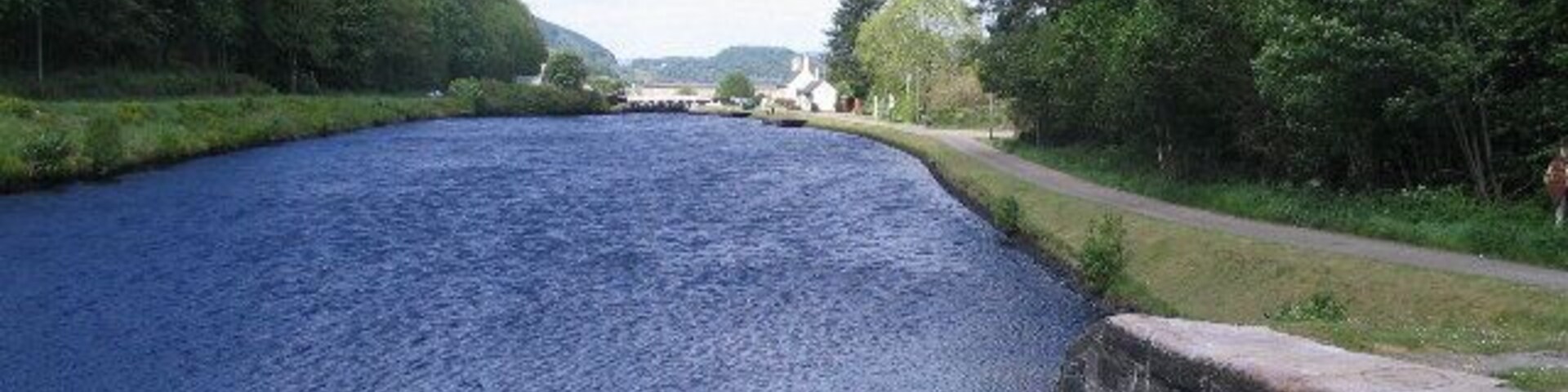 Un río tranquilo con un muro de piedra a un lado y una orilla cubierta de césped al otro.