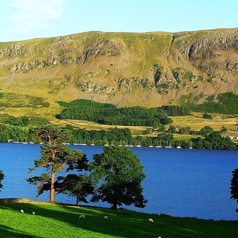A lake surrounded by green hills and a rocky mountain range.