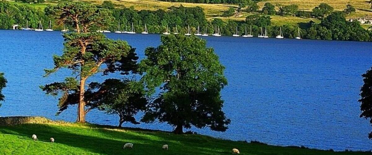 A lake surrounded by green hills and a rocky mountain range.