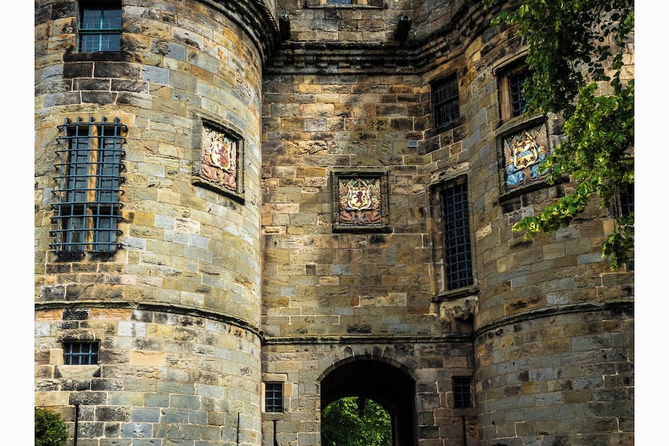 Een historisch stenen kasteel met een ronde toren, een rondboogvormige ingang en decoratieve ramen.