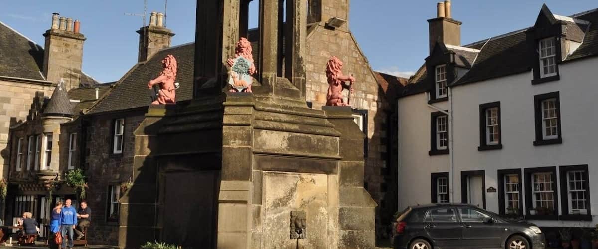 A stone tower with a weather vane, statues, and a flag on top.