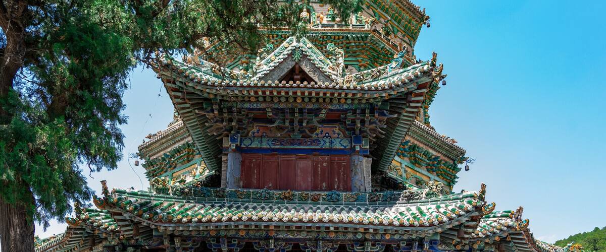 A traditional multi-tiered pagoda with ornate decorations and a large tree in the foreground.