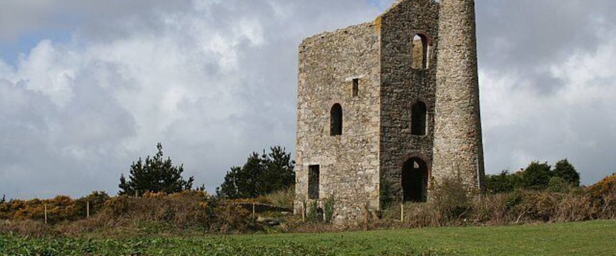 An old stone building with a chimney, surrounded by a grassy field and trees.