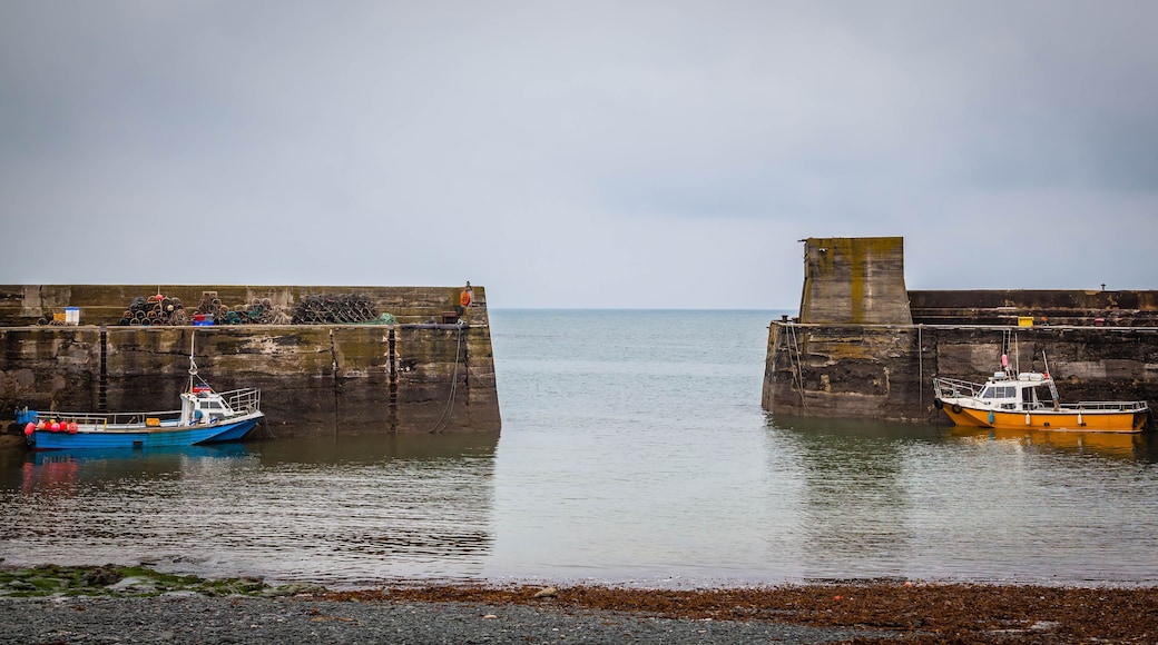 A harbor with two boats docked at a stone pier, calm water, and a cloudy sky.