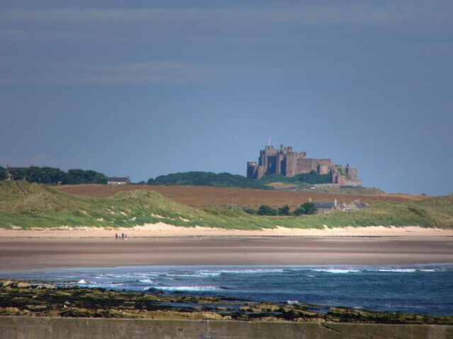 A coastal landscape with a castle on a hill, a sandy beach, and rocky shoreline.