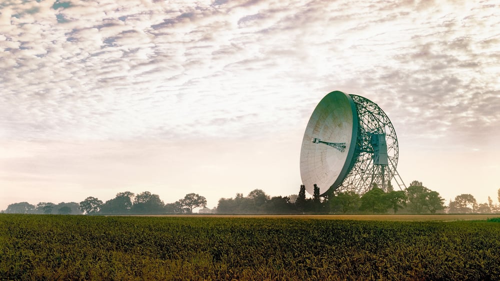 Une grande structure circulaire se dresse dans un champ, sous un ciel nuageux.