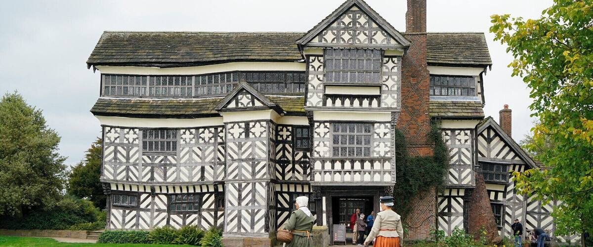 A Tudor-style building with a white and black timber-framed facade, a brick chimney, and a paved pathway leading to the entrance.