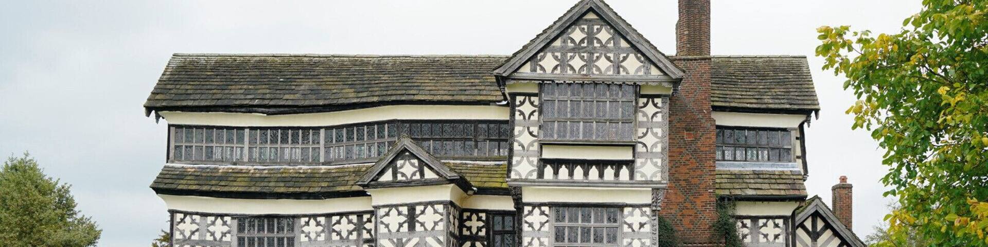A Tudor-style building with a white and black timber-framed facade, a brick chimney, and a paved pathway leading to the entrance.