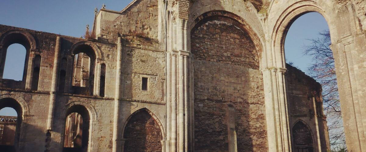 An ancient stone structure with large arches and columns, featuring weathered walls and remnants of statues.