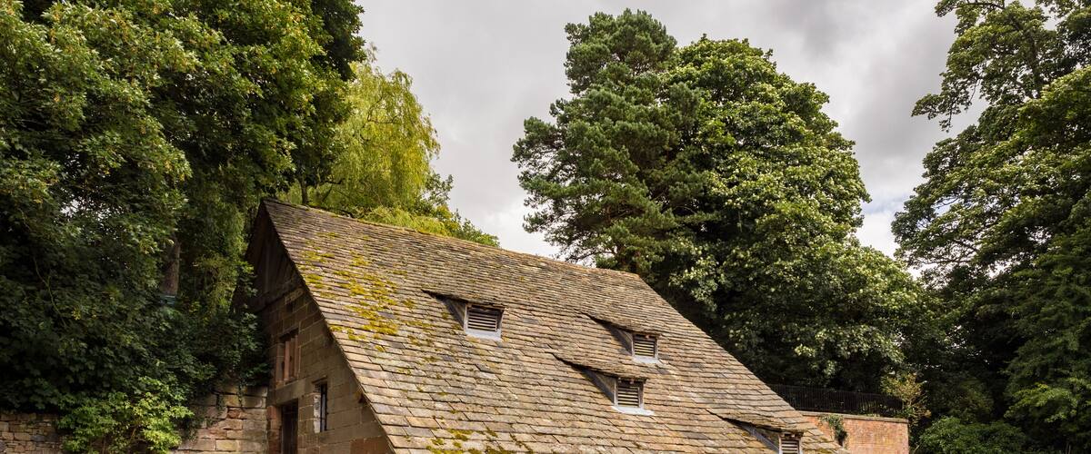 A stone house with a steeply pitched roof surrounded by lush greenery.