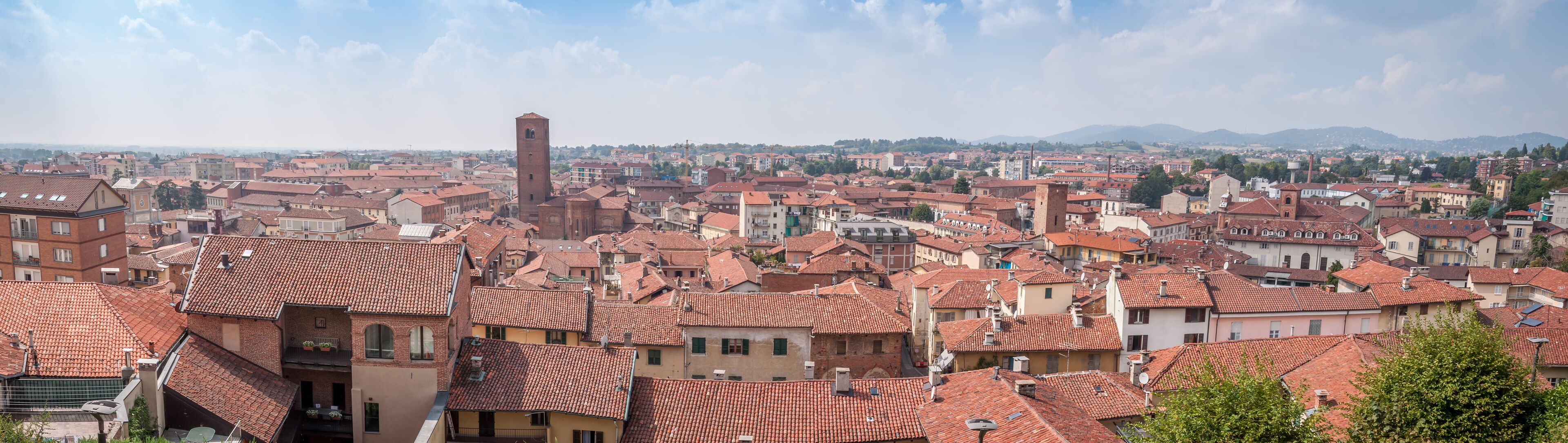 A cityscape with red-tiled roofs, a prominent tower, and a mountainous backdrop.