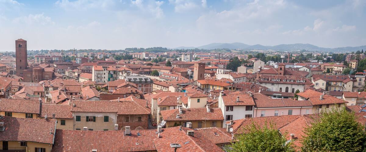 A cityscape with red-tiled roofs, a prominent tower, and a mountainous backdrop.