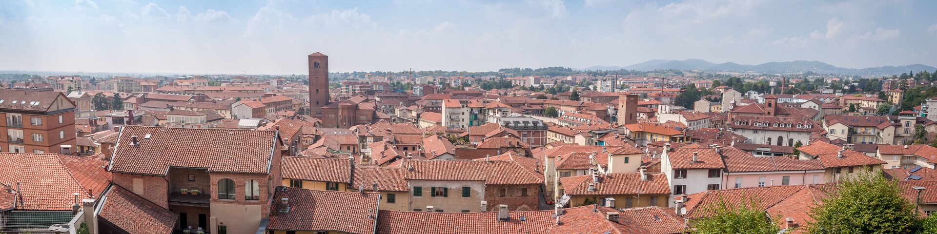 A cityscape with red-tiled roofs, a prominent tower, and a mountainous backdrop.