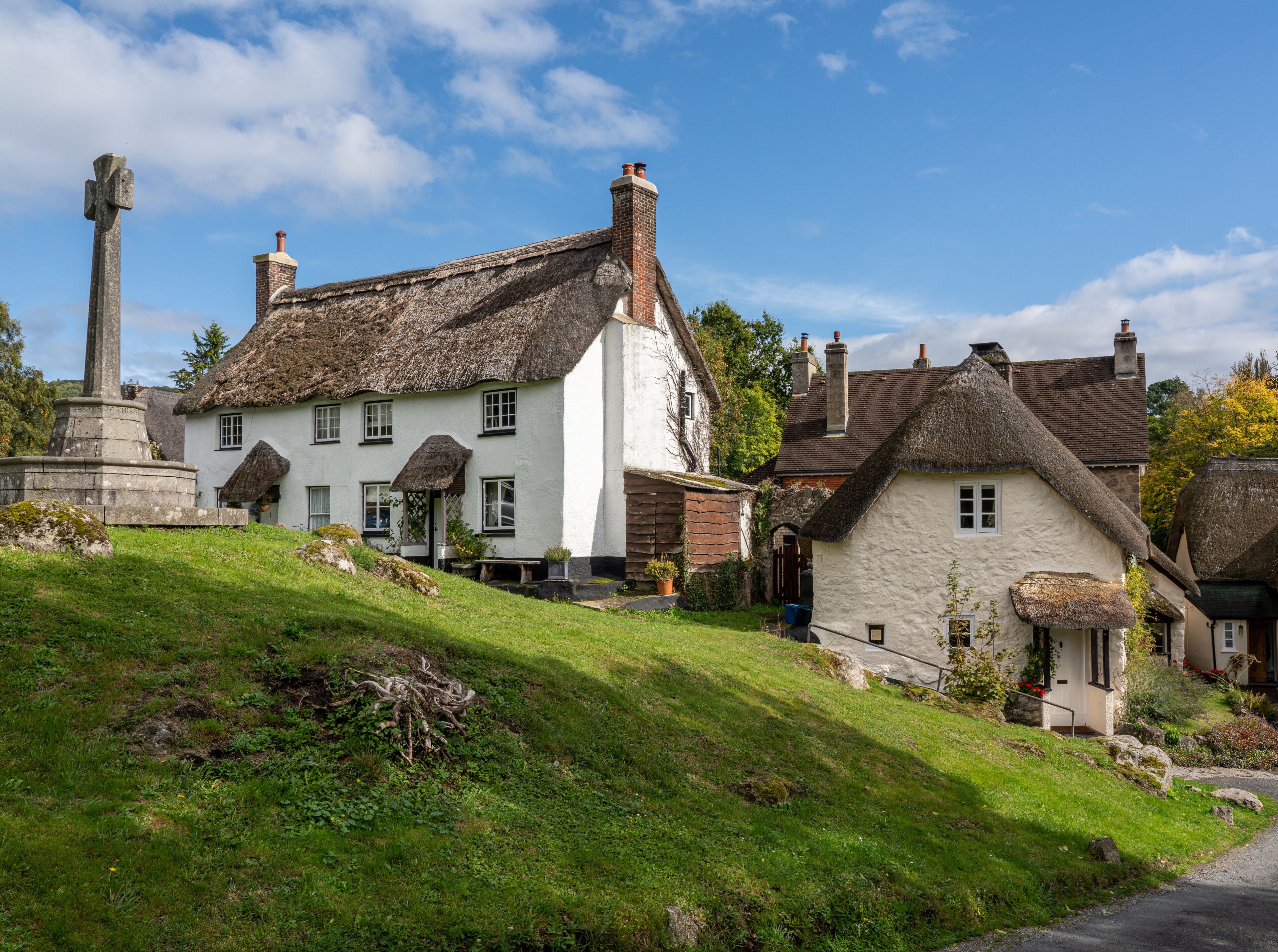 A traditional white house with a thatched roof, a stone monument, and a grassy hill.