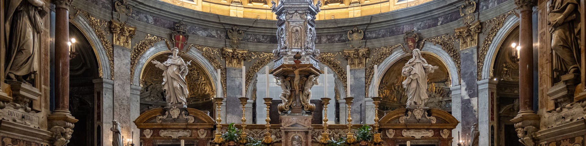 An ornate church interior with statues, a central altar, and a checkered floor.