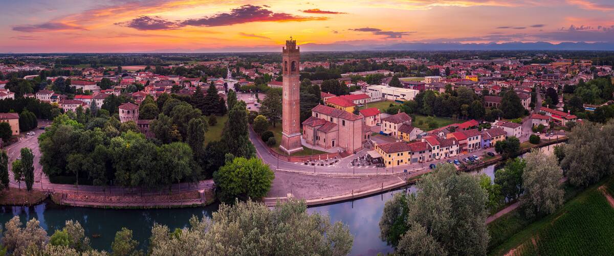 A town with a prominent tower, a river, and surrounding greenery.