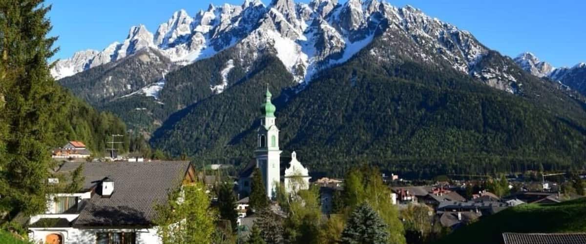 Una cordillera con picos nevados, una iglesia de techo verde y un pequeño pueblo en primer plano.
