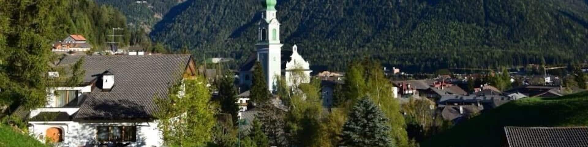 A mountain range with snow-capped peaks, a church with a green roof, and a small village in the foreground.