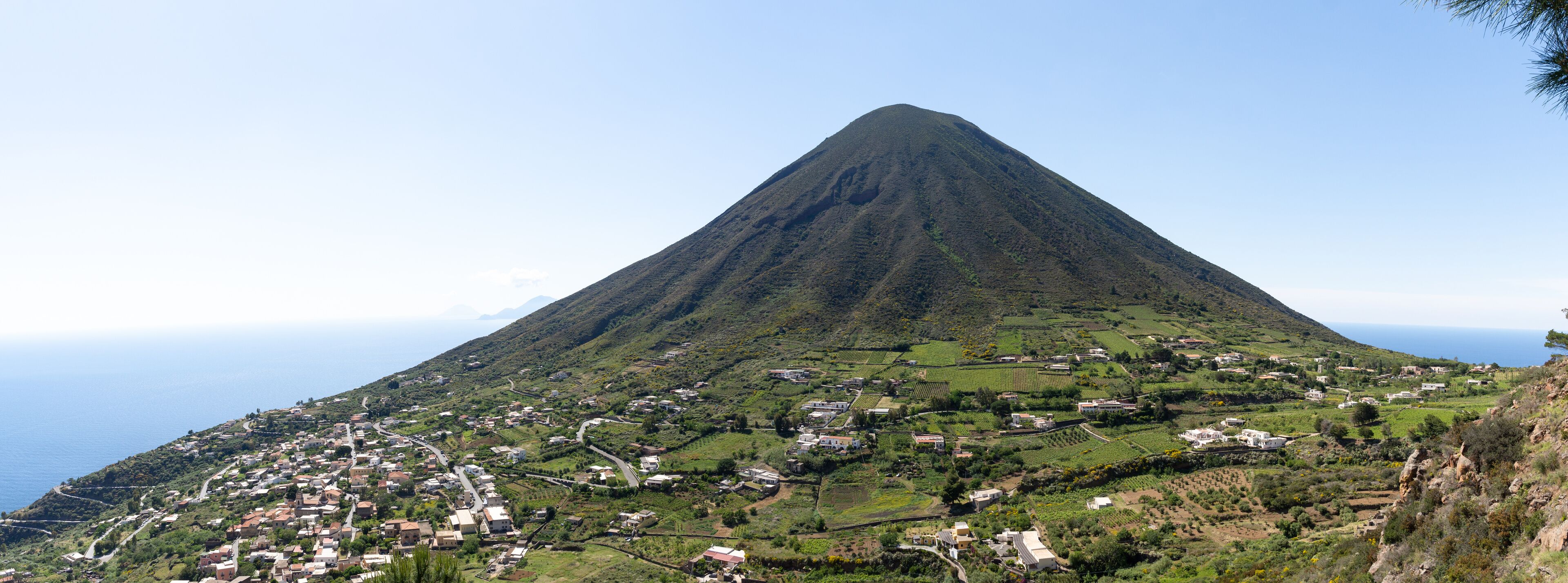 A mountain with a village at its base, surrounded by greenery and fields.