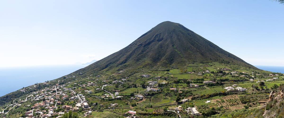 A mountain with a village at its base, surrounded by greenery and fields.