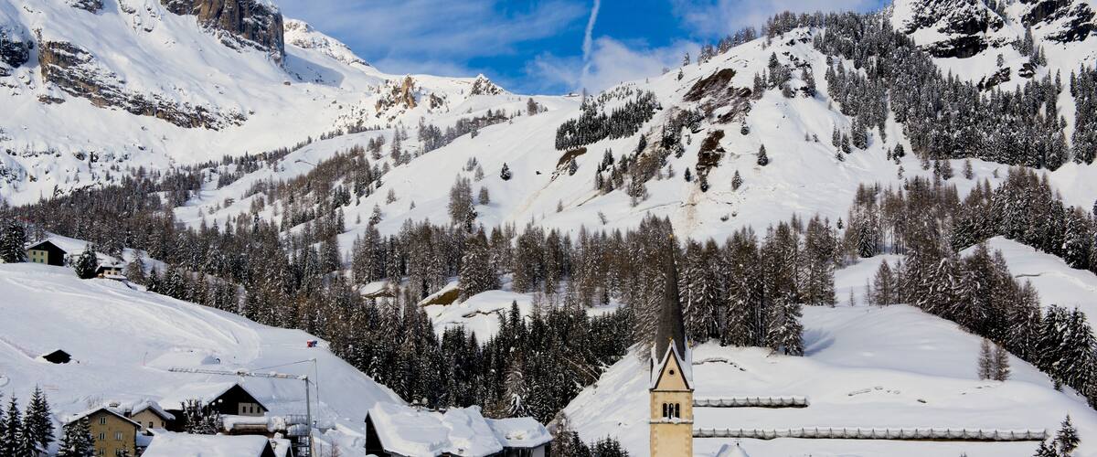 A snow-covered mountain village with buildings, a church, and a ski slope.