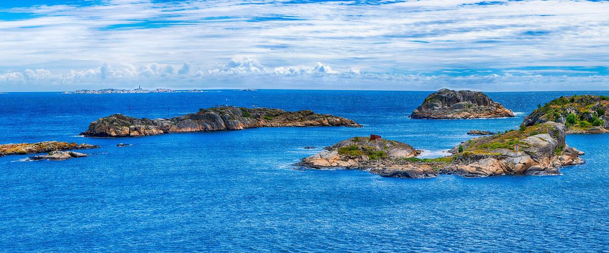 A coastal landscape with rocky islands and a lighthouse in the distance.