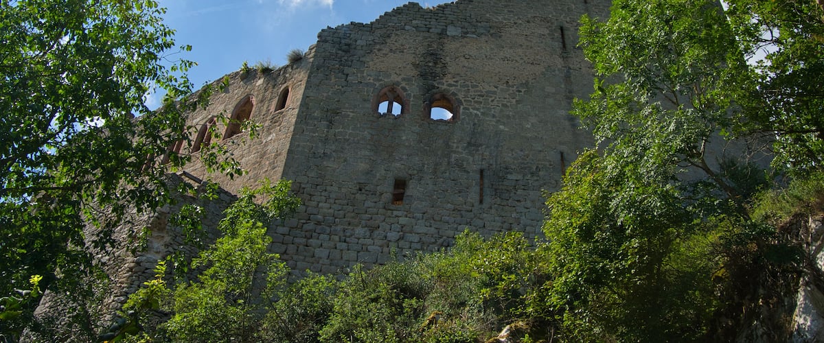 A historic stone castle with battlements, surrounded by lush greenery and a clear blue sky.