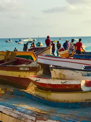 A row of small boats docked at a pier with people standing on them.