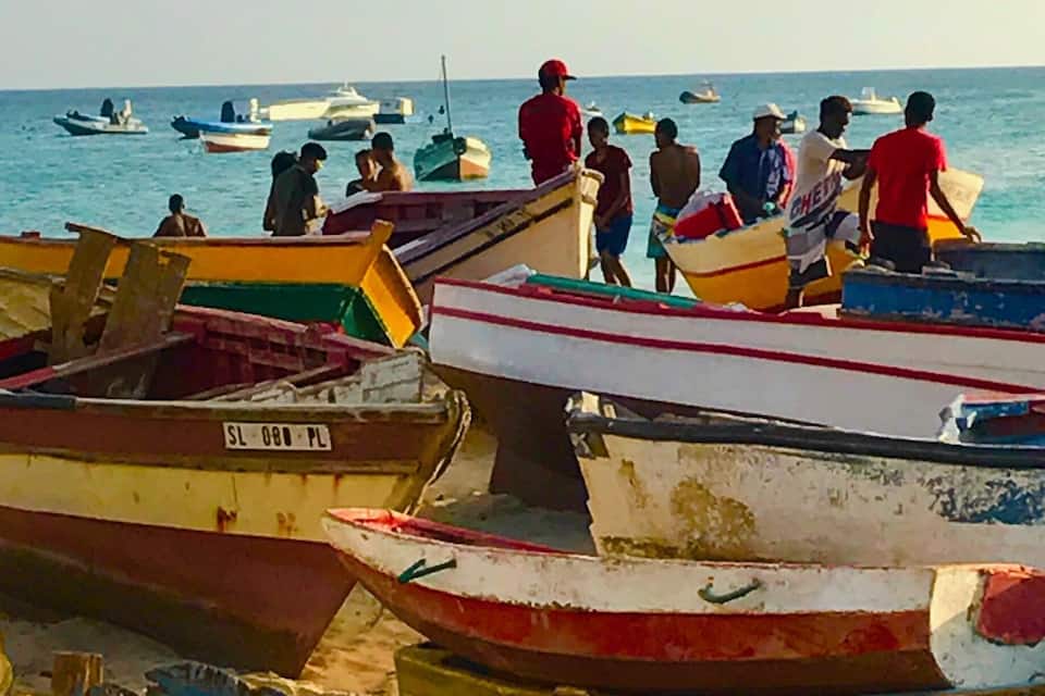 A row of small boats docked at a pier with people standing on them.