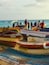 A row of small boats docked at a pier with people standing on them.