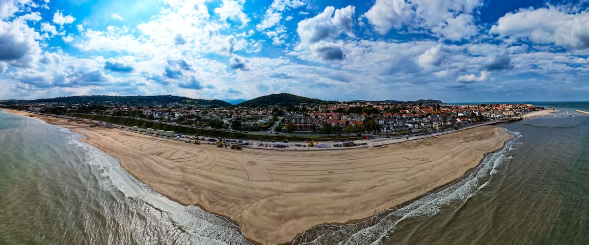 A coastal town with a beach, a harbor, and a hill in the background.